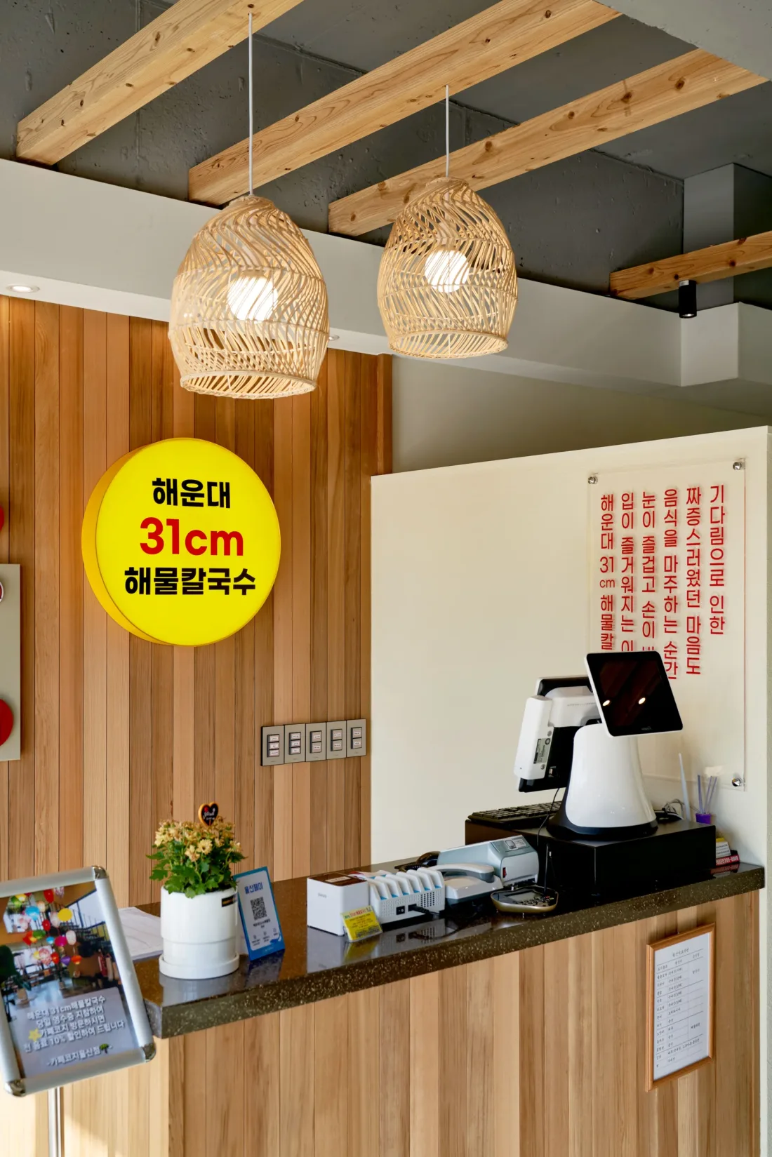 해운대31해물칼국수 울산동구점(울산 동구) 라탄 조명과 원목 마감을 적용한 주문 카운터 — 음식점 인테리어 시공 사례